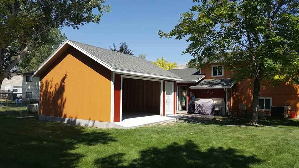 A detached orange garage with a gray gable roof and an open doorway, located in a grassy backyard near a house under the shade of nearby trees.