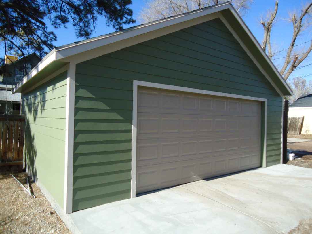 A green detached garage with beige trim and a matching beige garage door, featuring smooth lap siding and a gable roof, located in a residential backyard.