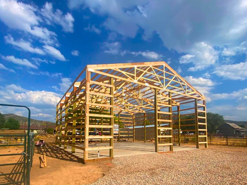 Unfinished pole barn structure with wooden framing set against a clear blue sky.