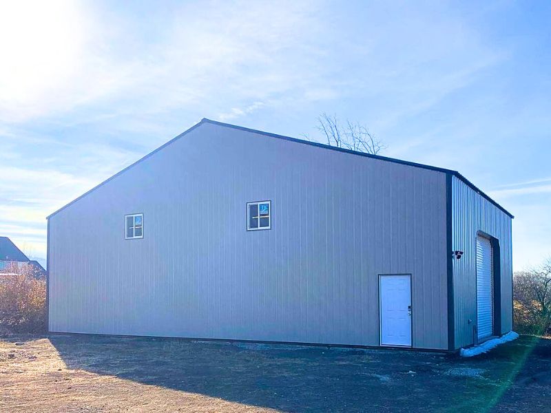 Exterior view of a modern metal building with two small windows, a door, and a large garage door under a clear blue sky.