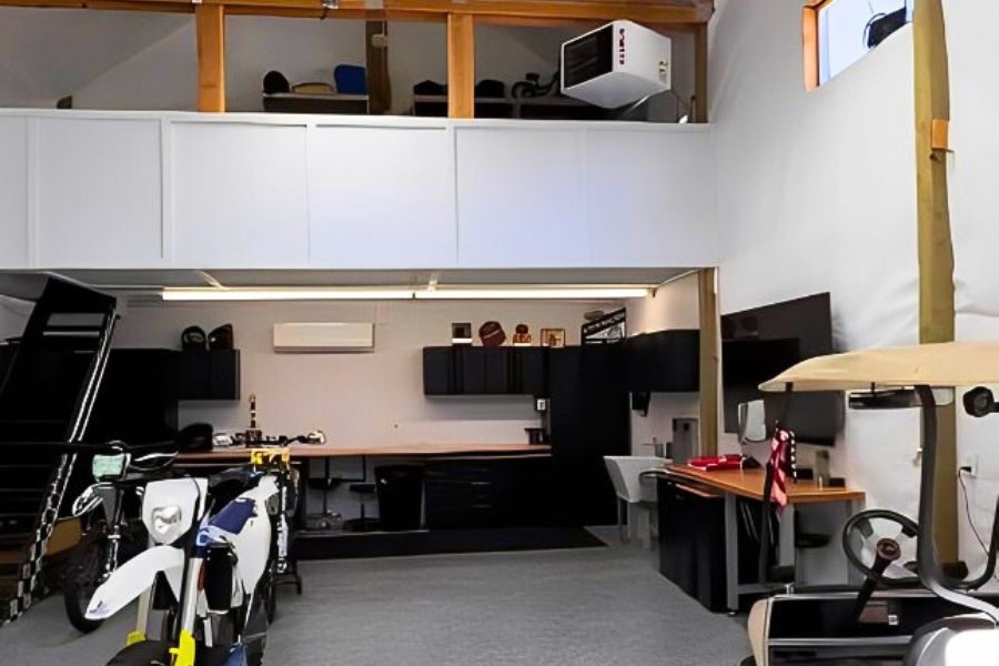 A spacious and modern garage with motorcycles, a golf cart, a loft area, and a sleek workstation featuring black cabinetry and ample lighting.