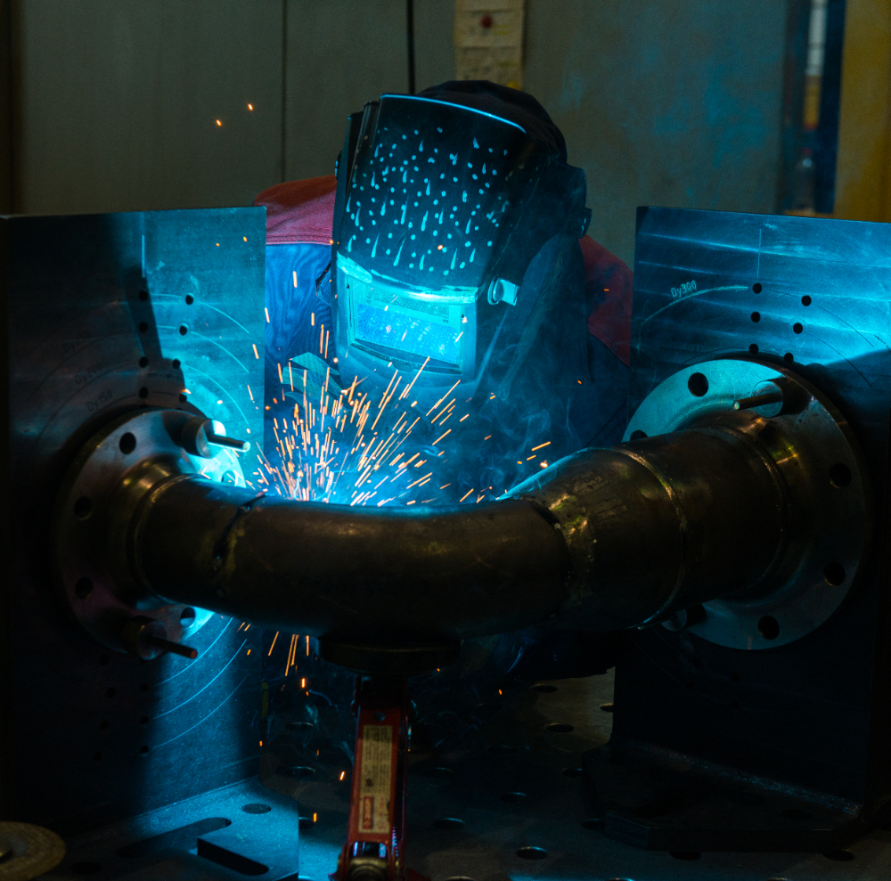 Welder using a helmet while working on a metal pipe with sparks illuminating the scene.